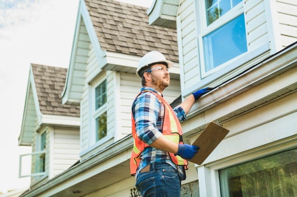 A man with a hard hat standing on steps fixing a roof on a house
