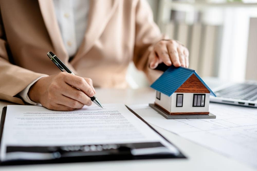 Real estate investor signing a fix and flip loan agreement with a model house on the table