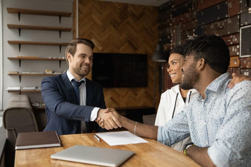Smiling real estate investors shaking hands with a loan officer after securing fix and flip financing.